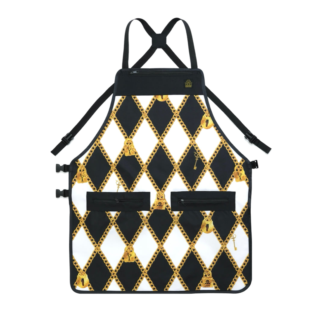 A black and white barber apron with a repeating diamond pattern outlined in gold, featuring two front pockets and adjustable cross back straps, shown against a plain white background.