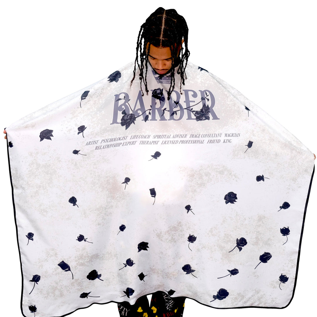 Person wearing a cape with 'BARBER' text and flower patterns on a white background