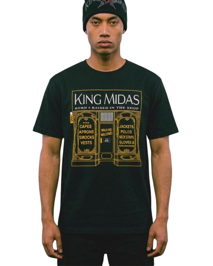 A man wearing a barber  black t-shirt with a gold graphic print that reads 'King Midas' and 'Born Raised in the Shop', paired with a black beanie against a plain white background.