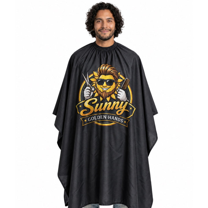 A man wearing a black custom barber cape with a large gold and yellow lion graphic that reads 'Sunny Golden Hands' on the front, set against a plain white background.