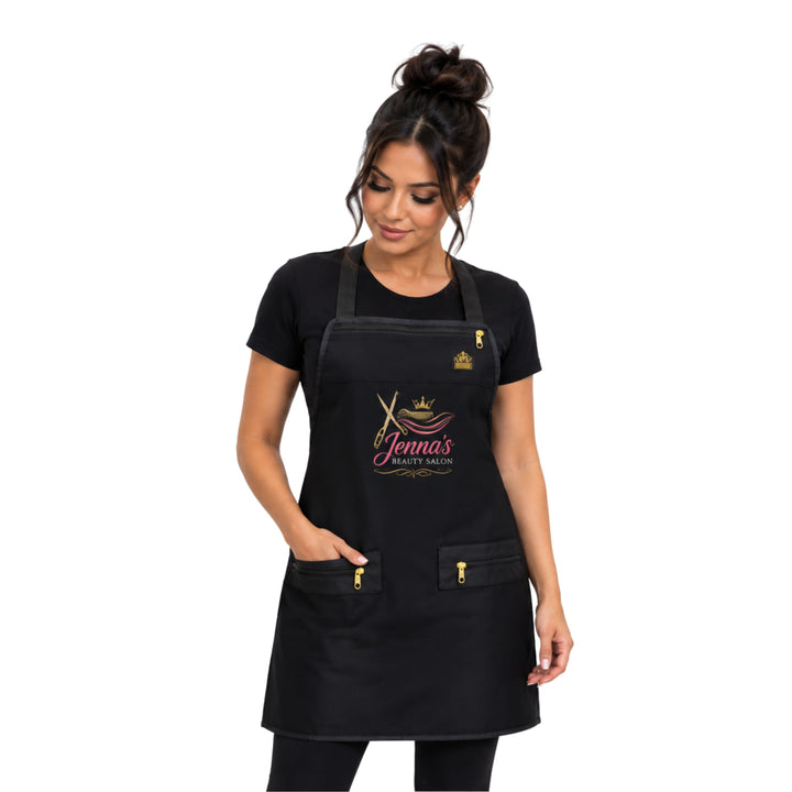 A woman modeling a black salon apron with gold and pink logo personalized hair stylist apron details on the front, featuring a neck strap, waist ties, and two front pockets with gold zippers.
