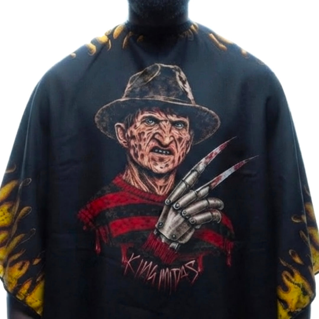 A black Halloween barber cape featuring a graphic print of Freddy Krueger with his signature red-and-black striped sweater, fedora, and metal clawed glove, plus yellow flame motifs on the sleeves.