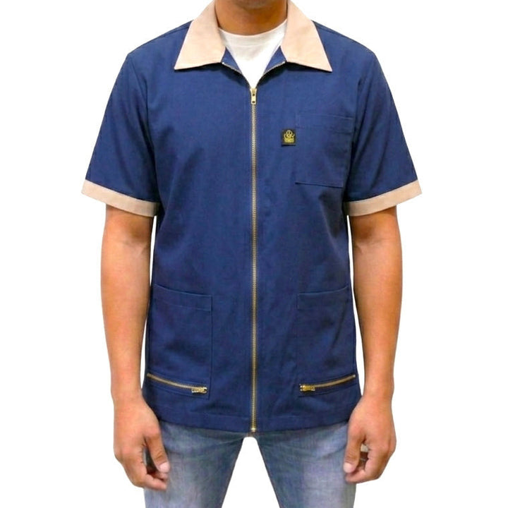 A man wearing a navy blue barber jacket / navy blue barber smock jacket with short-sleeves. 
