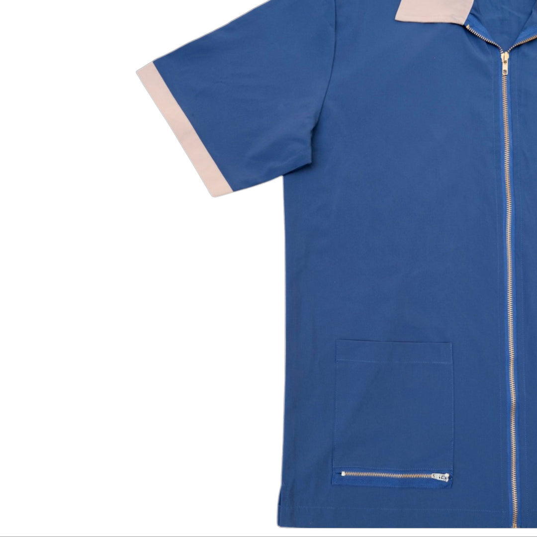 A blue short-sleeve utility scrub top with a front zipper, a zippered chest pocket, and light beige contrast trim on the collar and sleeve cuffs, shown against a plain white background.