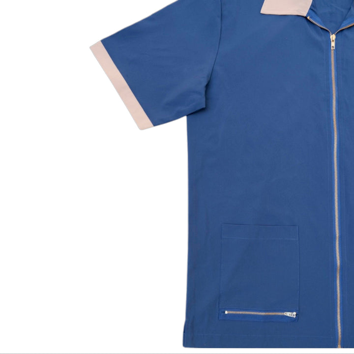 A blue short-sleeve utility scrub top with a front zipper, a zippered chest pocket, and light beige contrast trim on the collar and sleeve cuffs, shown against a plain white background.