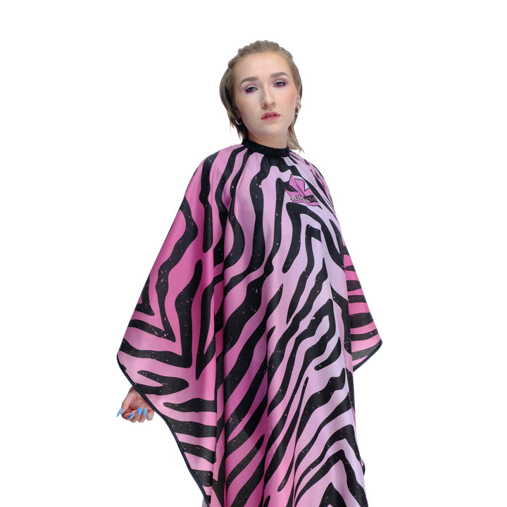 Person wearing a pink and black zebra hair stylist cape with a logo. 
Salon cape - hair stylist cape - zebra print hair stylist cape- pink hair stylist cape