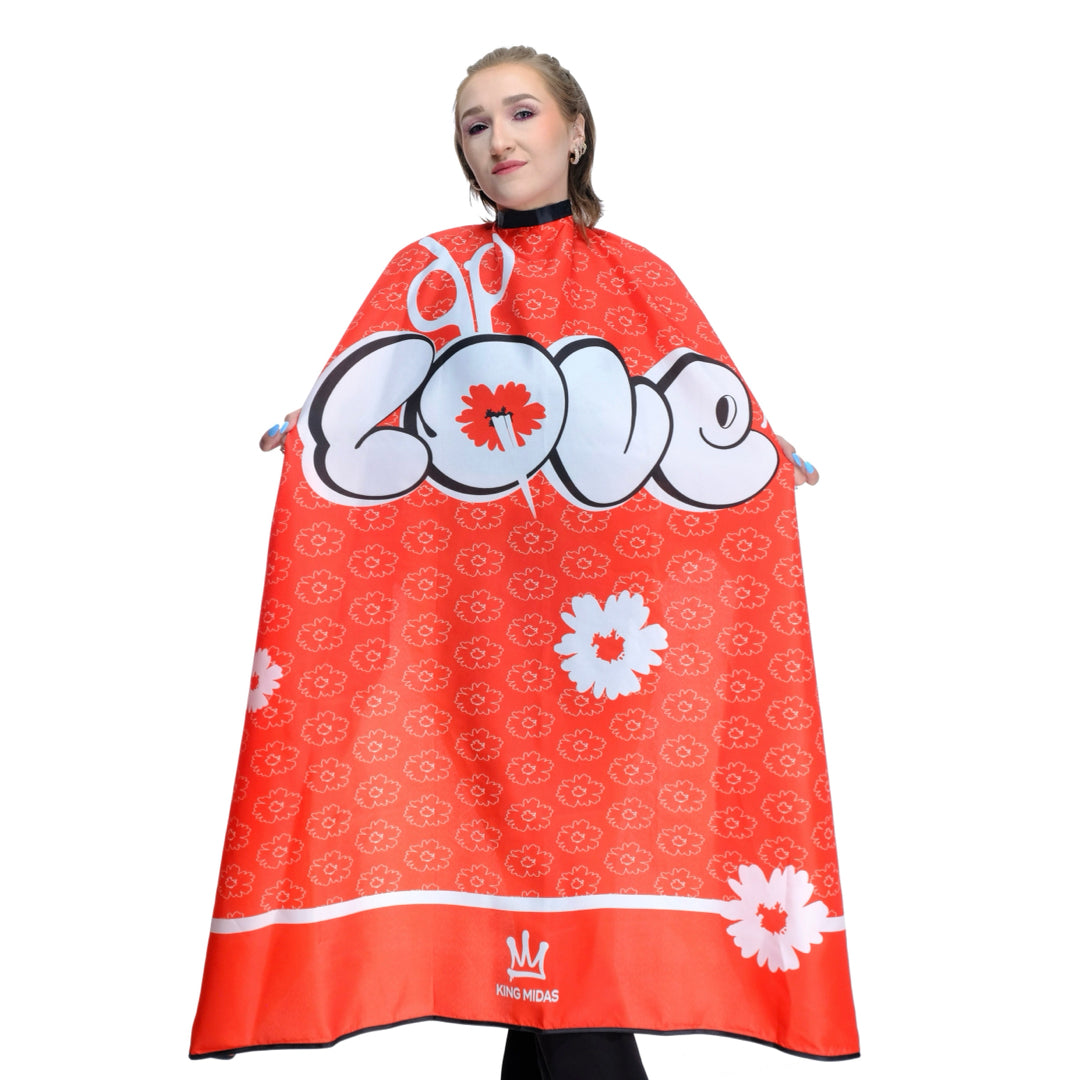 Person wearing a red  hairdressing cape or barber cape with floral patterns and a visible love graffiti logo. Barber cape- barber capes- barber cape for men- love barber cape- capes for barber