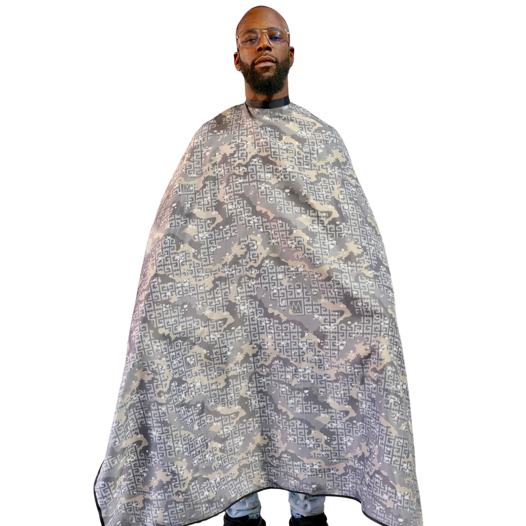 A man wearing a large barber-style cape with a gray, beige, and white camouflage pattern featuring Greek key motifs, shown against a plain white background.