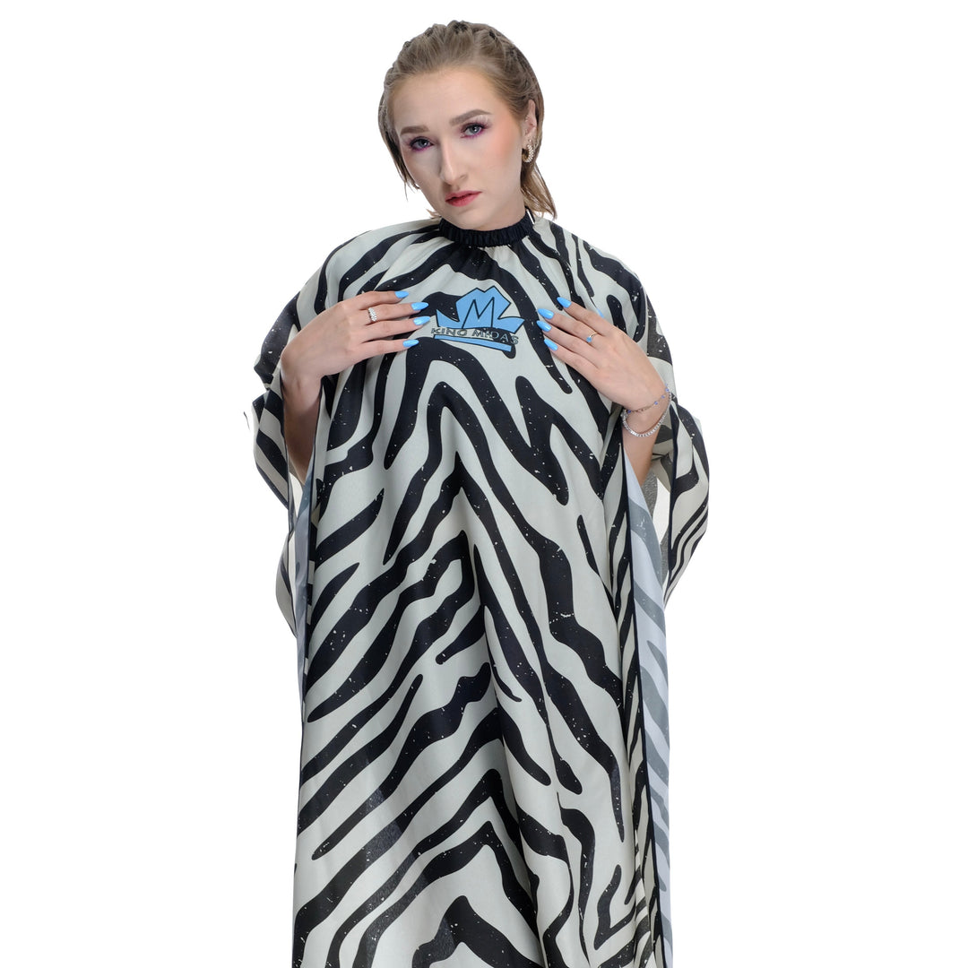Person wearing a zebra patterned hair stylist cape over a black outfit on a white background