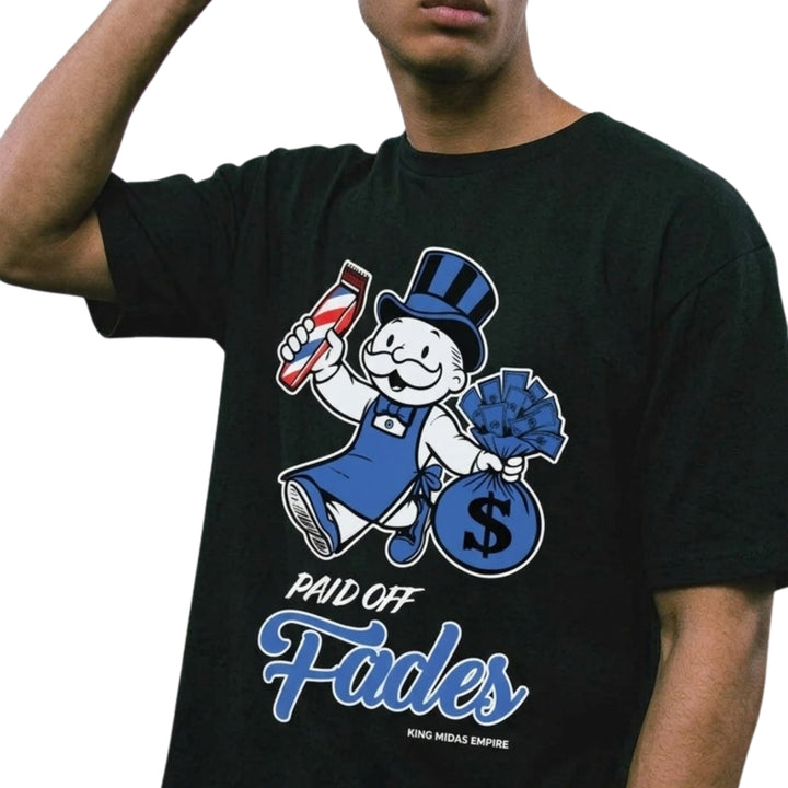 A man wearing a black graphic t-shirt with a cartoon mascot and the text 'PAID OFF Fades' in blue and white, against a plain white background.