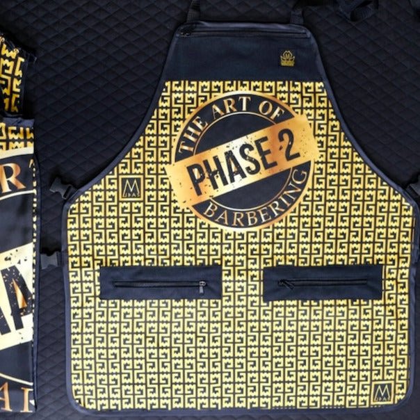 Barber apron with 'The Art of Phase 2 Barbering' logo on a yellow and black patterned background.