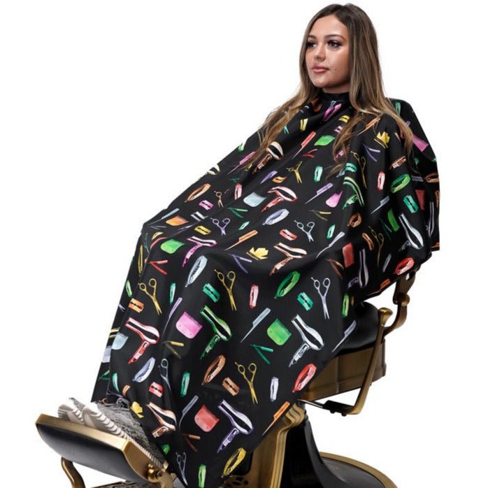 Woman sitting in a barber chair with a colorful salon cape draped over her.