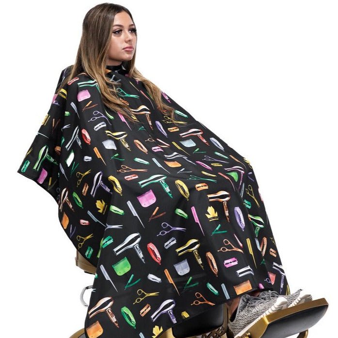 Person wearing a black hairdressing cape with colorful tool patterns on a white background