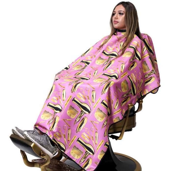 Person sitting in a salon chair with a pink cape featuring gold hairdressing tools on a white background
